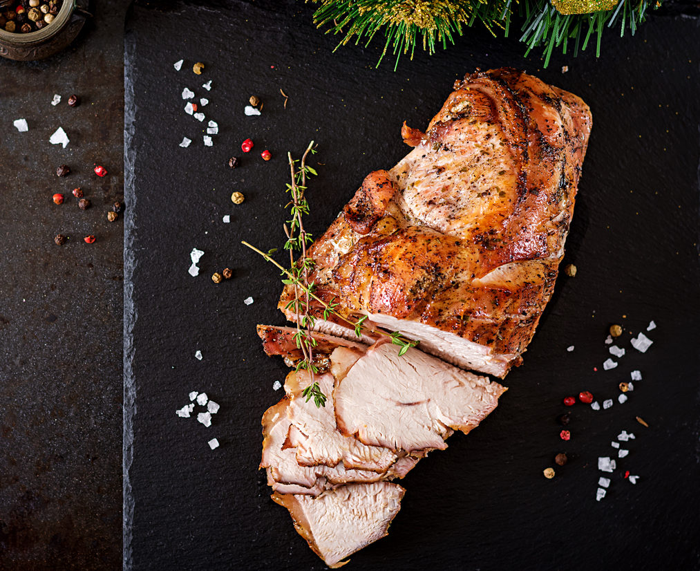 Roasted sliced Christmas ham of turkey on dark rustic background. Top view. Festival food.